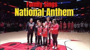 Announcer: SINGING THE NATIONAL ANTHEM THE SHARPE FAMILY SINGERS! All: Oh say, can you see... (line from the Sharpe Family Singers singing the national anthem in Chicago with Benny the Bull)